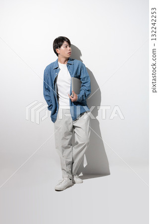 A young man in denim holding a laptop. Full-body image of an engineer, designer, or freelancer. 132242253