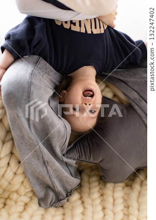 A child is held upside down, smiling and laughing. The child is wearing a sweatshirt and gray sweatpants. 132247402