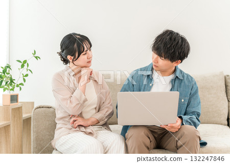 A young Asian couple sitting on the sofa in the living room talking and consulting while looking at a computer, a married couple A young Asian couple sitting on the sofa in the living room talking and consulting while looking at a computer, a married couple 132247846