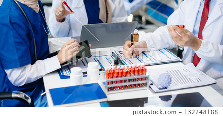 Medical team having a meeting with doctors in white lab coats and surgical scrubs seated at a table discussing a patients working Medical team having a meeting with doctors in white lab coats and surgical scrubs seated at a table discussing a patients working 132248188