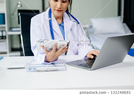 Beautiful physician doctor sit on table in office hospital. Attractive therapist female practitioner pharmacist smile and use tablet and laptop. Beautiful physician doctor sit on table in office hospital. Attractive therapist female practitioner pharmacist smile and use tablet and laptop. 132248691