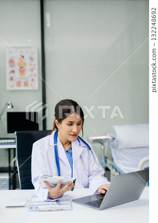 Beautiful physician doctor sit on table in office hospital. Attractive therapist female practitioner pharmacist smile and use tablet and laptop. Beautiful physician doctor sit on table in office hospital. Attractive therapist female practitioner pharmacist smile and use tablet and laptop. 132248692
