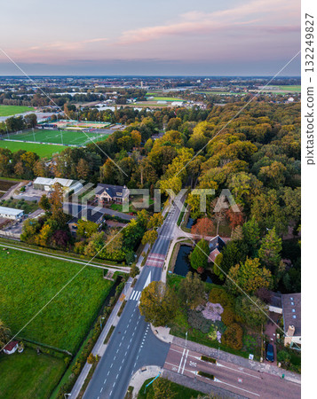 Aerial view of residential neighborhood rows of houses with gardens, central green park, curved road, and open grassy fields, showcasing organized urban planning and integrated public space. Aerial view of residential neighborhood rows of houses with gardens, central green park, curved road, and open grassy fields, showcasing organized urban planning and integrated public space. 132249827