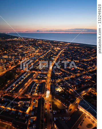 Aerial view of coastal city at dusk streetlights and building lights form glowing networks, sea meets horizon under orange blue sky, blending urban structure with natural sunset beauty. Aerial view of coastal city at dusk streetlights and building lights form glowing networks, sea meets horizon under orange blue sky, blending urban structure with natural sunset beauty. 132249828