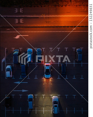 Aerial nighttime view of empty parking lot warm orange streetlights illuminate marked lanes and scattered cars, highlighting symmetry Aerial nighttime view of empty parking lot warm orange streetlights illuminate marked lanes and scattered cars, highlighting symmetry 132249831