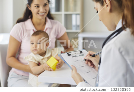 Doctor reviewing family therapy form with mother and baby during clinic visit 132250595