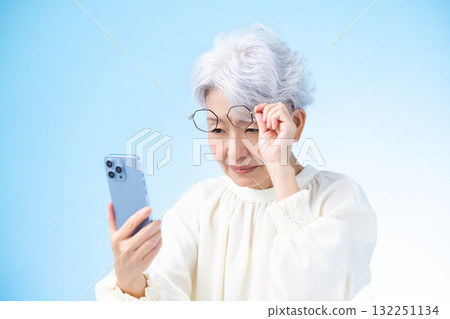 Presbyopia Senior woman looking at smartphone with glasses shifted Presbyopia Senior woman looking at smartphone with glasses shifted 132251134