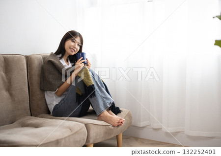 Young woman enjoying a hot drink under a blanket by the window 132252401