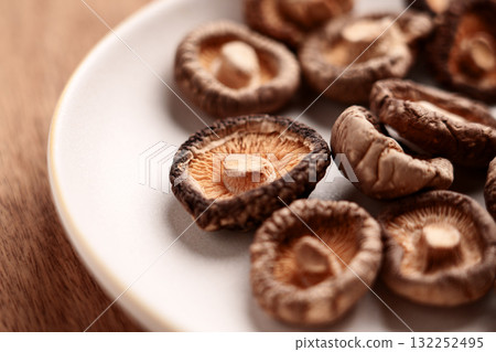 Dried shriveled edible shiitake mushrooms in ceramic bowl on wooden table. Dehydrated nutritious ingredient 132252495
