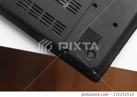 Upside down black laptop with cooling vents and screw mounts on white table 132252519