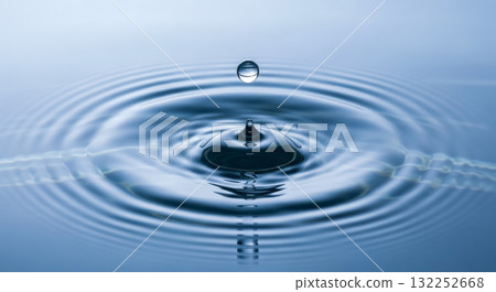 Water drop falling on calm blue water surface creating ripples for concept of purity, clarity, zen, meditation and wellness 132252668