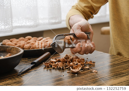Hand using a nutcracker to break open walnuts on a wooden table in a cozy kitchen setting Hand using a nutcracker to break open walnuts on a wooden table in a cozy kitchen setting 132252759