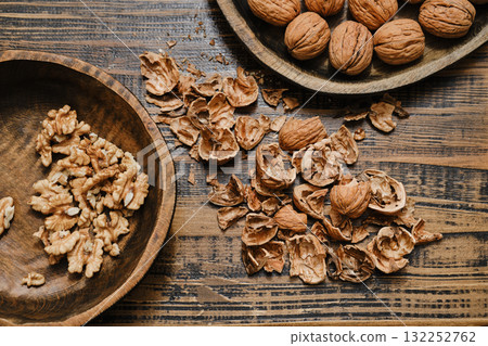 Various walnuts, broken shells, and walnut pieces on wooden table create a rustic kitchen scene 132252762