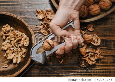 Hand using a nutcracker to break open a walnut on a wooden table 132252763