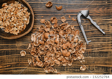 Walnuts being shelled on wooden surface with tools and bowl beside them Walnuts being shelled on wooden surface with tools and bowl beside them 132252764