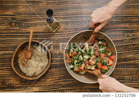 Fresh vegetable salad preparation on a rustic wooden table with garnishing ingredients nearby Fresh vegetable salad preparation on a rustic wooden table with garnishing ingredients nearby 132252786