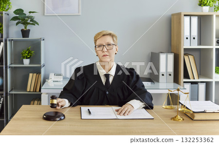 Female judge signing legal documents at courtroom desk with gavel and scales Female judge signing legal documents at courtroom desk with gavel and scales 132253362