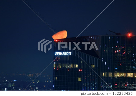 Early half harvest moon in Tokyo over the new Takanawa Gateway Marriott Hotel in the early evening in Minato-ku Tokyo Japan 132253425