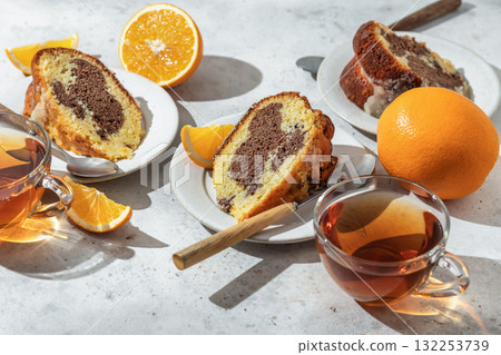 Piece of orange and chocolate marble bundt cake in bright morning light close up. Fruity citrus dessert on light gray kitchen background 132253739