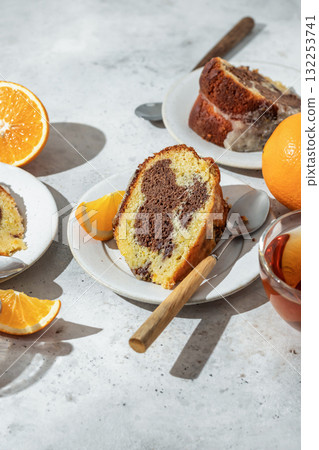 Piece of orange and chocolate marble bundt cake in bright morning light close up. Fruity citrus dessert on light gray kitchen background Piece of orange and chocolate marble bundt cake in bright morning light close up. Fruity citrus dessert on light gray kitchen background 132253741