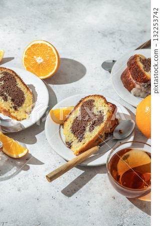 Piece of orange and chocolate marble bundt cake in bright morning light. Fruity citrus dessert on light gray kitchen background, text space Piece of orange and chocolate marble bundt cake in bright morning light. Fruity citrus dessert on light gray kitchen background, text space 132253742
