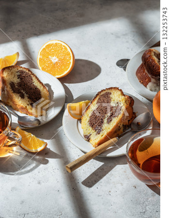 Piece of orange and chocolate marble bundt cake in bright morning light with clear window shadows. Fruity citrus dessert on light gray kitchen background Piece of orange and chocolate marble bundt cake in bright morning light with clear window shadows. Fruity citrus dessert on light gray kitchen background 132253743