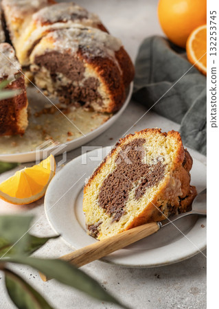 Piece of orange and chocolate marble bundt cake with sugar icing close up. Fruity citrus dessert on light gray kitchen background Piece of orange and chocolate marble bundt cake with sugar icing close up. Fruity citrus dessert on light gray kitchen background 132253745