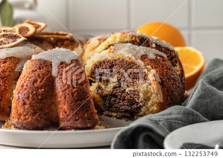 Sliced orange and chocolate bundt cake with sugar icing. Fruity citrus dessert on light gray kitchen background 132253749