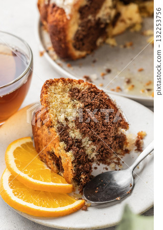 Piece of orange and chocolate marble bundt cake with sugar icing close up. Fruity citrus dessert on light gray kitchen background 132253756
