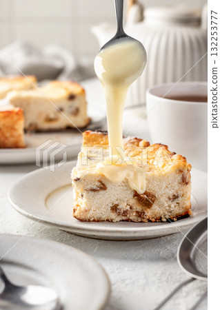 A piece of homemade cottage cheese casserole with raisins, process of pouring condensed milk on top. Baked cheesecake for breakfast on white table background 132253777