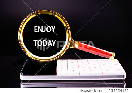 A golden magnifying glass rests on a sleek white surface, highlighting the words Enjoy Today in bold letters. This scene inspires mindfulness and appreciation for the present A golden magnifying glass rests on a sleek white surface, highlighting the words Enjoy Today in bold letters. This scene inspires mindfulness and appreciation for the present 132254181