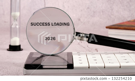 A magnifying glass focused on the words success loading with a future date of 2026 rests on a sleek black calculator, surrounded by an hourglass and books, symbolizing aspiration and time A magnifying glass focused on the words success loading with a future date of 2026 rests on a sleek black calculator, surrounded by an hourglass and books, symbolizing aspiration and time 132254210