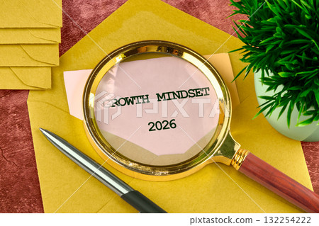 A magnifying glass highlights the words growth mindset 2026 on a note surrounded by stationery and a small plant, symbolizing focus and inspiration for future possibilities 132254222