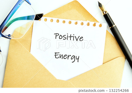 In a bright workspace, a handwritten note reading Positive Energy peeks out of a simple envelope. Nearby, glasses and a pen suggest a moment of inspiration and creativity 132254266