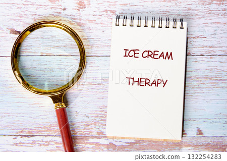 A notepad with the words ice cream therapy sits beside a magnifying glass on a rustic wooden table 132254283