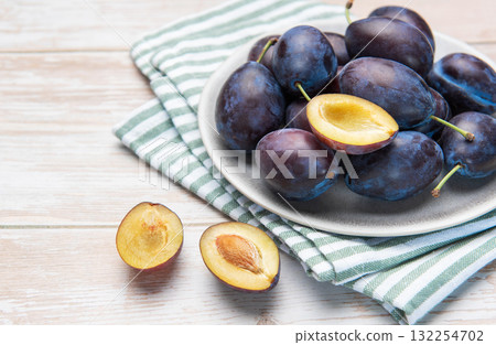 Fresh ripe plums in grey bowl on wood table 132254702