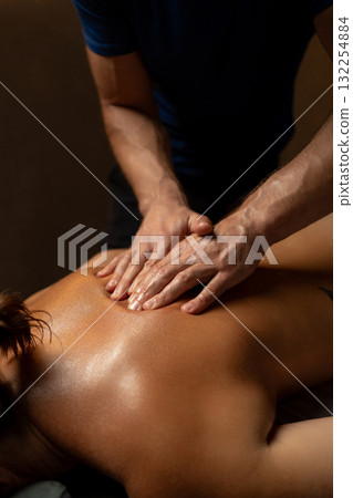 Close-up of a professional therapist performing a relaxing back massage in a spa setting, applying oil and pressure to relieve muscle tension and promote relaxation and wellbeing. 132254884
