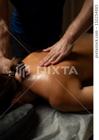 Close-up of a professional therapist performing a relaxing back massage in a spa setting, applying oil and pressure to relieve muscle tension and promote relaxation and wellbeing. 132254885