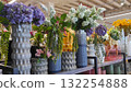 Colorful floral arrangements in various textured vases displayed on a modern shelf, showcasing vibrant blooms and greenery in a contemporary retail environment 132254888