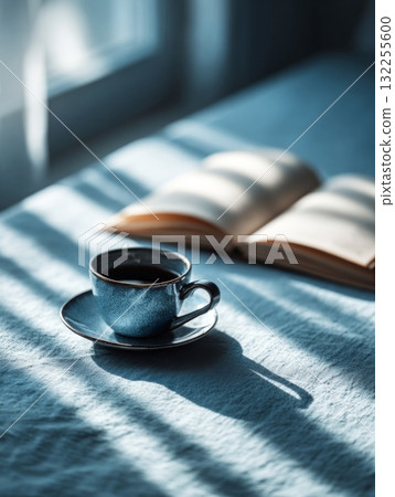 Blue cup of coffee and book enjoying calm morning light 132255600