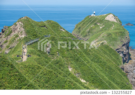 Tourists hiking on green cliffs near lighthouse by the ocean on sunny day at Cape Kamui, Kozakicho, Hokkaido, Japan 132255827