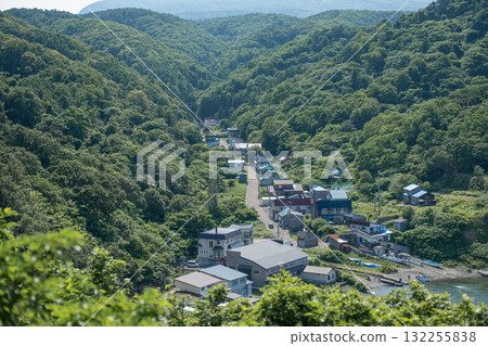 Small village nestled in green forested hills near river in rural landscape Cape Ogon, Shakotan, Hokkaido, Japan 132255838