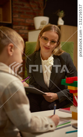 Psychologist smiling at boy drawing with colored pencils during therapy with toy blocks Psychologist smiling at boy drawing with colored pencils during therapy with toy blocks 132256537