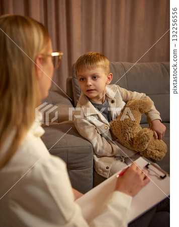 Boy holding teddy bear during therapy conversation with psychologist in calm atmosphere 132256556