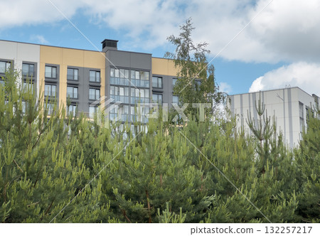 Apartment building blends with nature. Modern residential facade surrounded by pine trees shows eco Apartment building blends with nature. Modern residential facade surrounded by pine trees shows eco 132257217