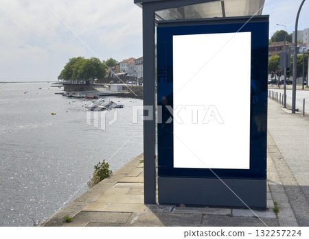 Billboard sign stands at waterfront bus station. Blank modern vertical panel with glass frame offers Billboard sign stands at waterfront bus station. Blank modern vertical panel with glass frame offers 132257224