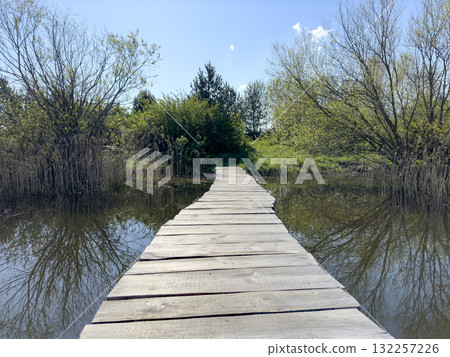 Bridge crosses tranquil pond in rural landscape. Wooden footbridge with plank pathway reflects in Bridge crosses tranquil pond in rural landscape. Wooden footbridge with plank pathway reflects in 132257226