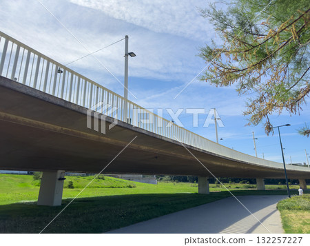 Bridge spans urban landscape. Modern concrete viaduct structure supports pedestrian pathway and road Bridge spans urban landscape. Modern concrete viaduct structure supports pedestrian pathway and road 132257227