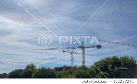 Construction cranes tower over expanding skyline. Urban development climbs beside summer park trees, Construction cranes tower over expanding skyline. Urban development climbs beside summer park trees, 132257275