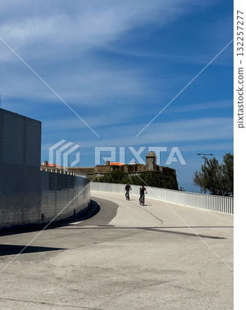 Cycling on bicycles in historic coastal city. Two cyclists ride down concrete road slope near Cycling on bicycles in historic coastal city. Two cyclists ride down concrete road slope near 132257277